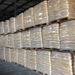 Magazyn wypełniony paletami z zapakowanym w folię pelletem, widoczne rzędy ułożone jeden na drugim, oświetlenie magazynowe.