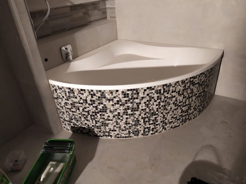 Narożna wanna obudowana mozaiką w odcieniach szarości i bieli, widoczna z perspektywy podłogi, z narzędziami glazurniczymi w tle, Gdańsk.