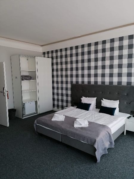 Pokój hotelowy z łóżkiem dwuosobowym, szafą z mini-lodówką i ścianą w czarno-białą kratę.