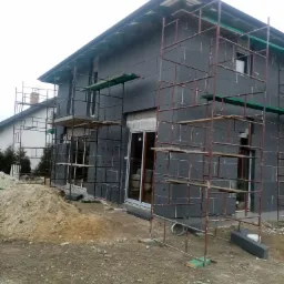 Dom w trakcie ocieplania styropianem grafitowym, widoczne rusztowania i fragment sąsiedniego domu.