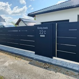 AL-DO Piotr Haśkiewicz - Nowoczesna, antracytowa brama wjazdowa z numerem posesji 'Kolejowa 22 C' na tle domu z ciemną dachówką i błękitnego nieba z chmurami. Minimalistyczny design.