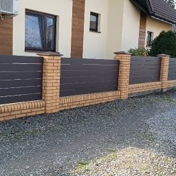AL-DO Piotr Haśkiewicz - Nowoczesne ogrodzenie posesji z poziomych, szarych paneli, wsparte na ceglanych słupkach i podmurówce, na tle domu z klimatyzatorem i żwirowego podjazdu.