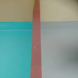 Wnętrze z pomalowanymi ścianami w trzech kolorach: beżowym, turkusowym i szarym, z pionowym pasem brązowych płytek przy suficie.