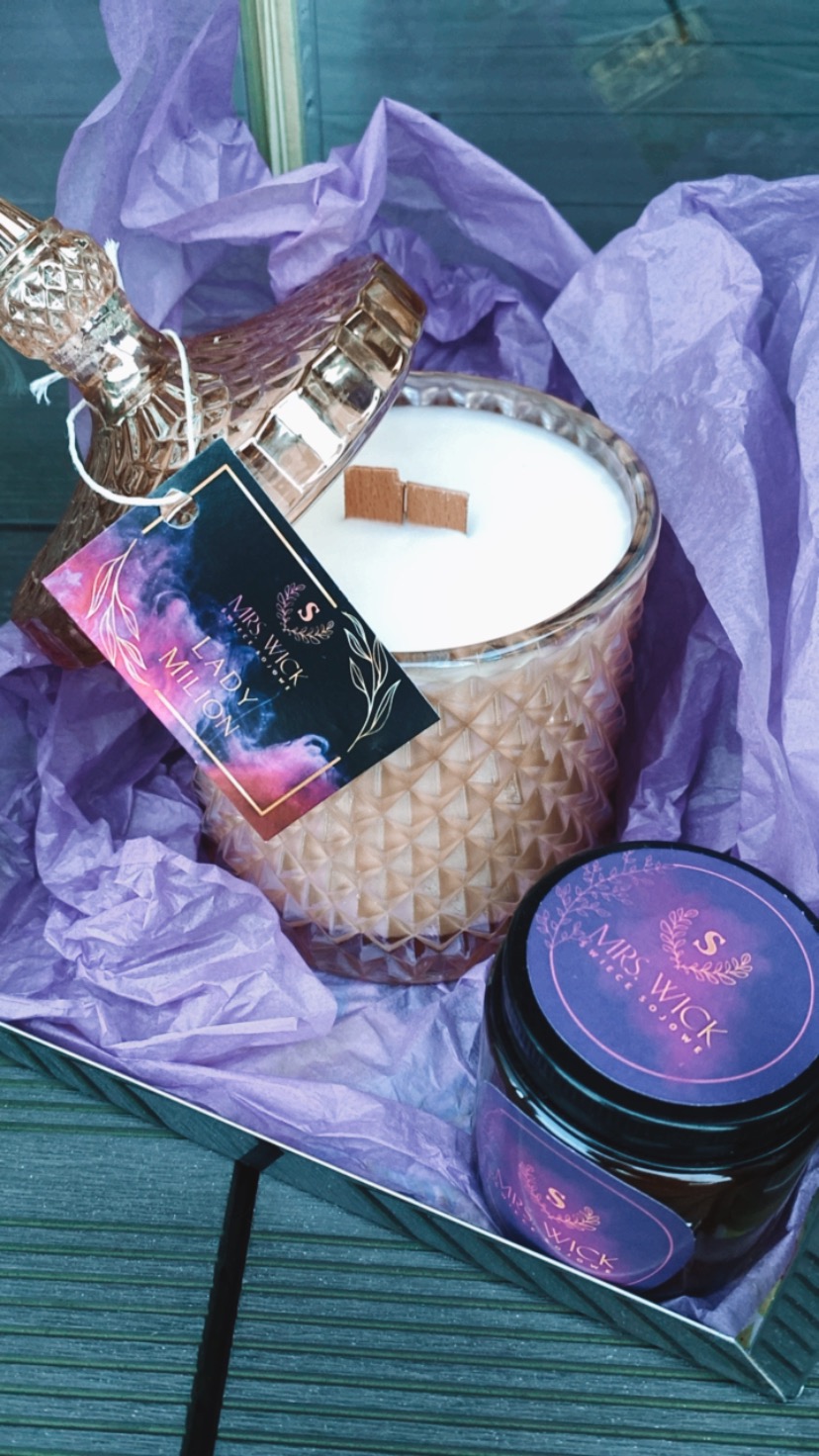 Otwarty słoik z woskiem sojowym i drewnianym knotem, etykieta 'Mrs. Wick Lady Milion', mniejszy słoik obok, fioletowa bibułka w srebrnym pudełku.
