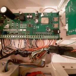 Otwarta obudowa centrali alarmowej Satel Perfecta 16A z widoczną płytą główną, licznymi przewodami podłączonymi do listwy zaciskowej i elementami elektroniki.