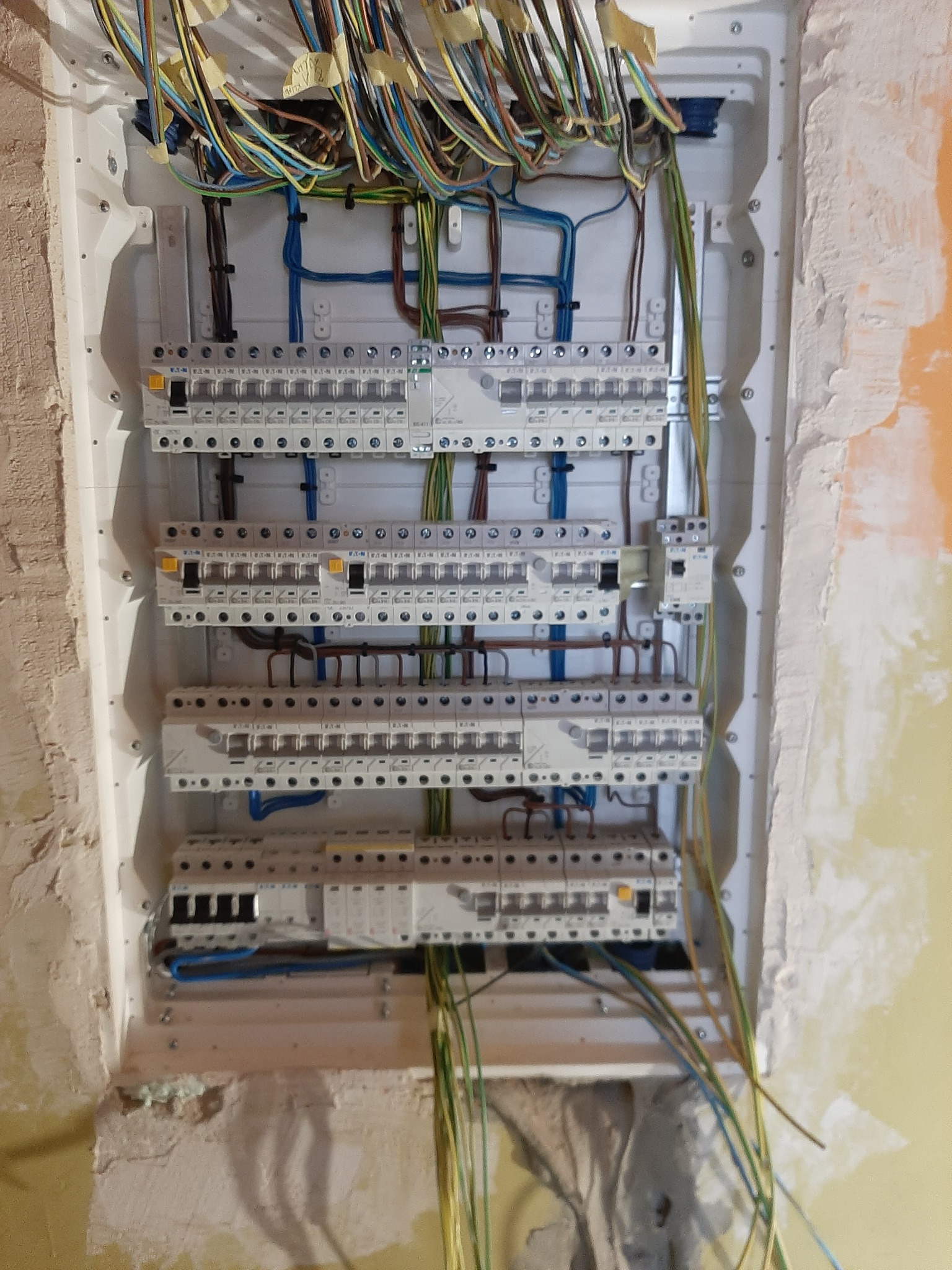 Rozdzielnica elektryczna z widocznymi bezpiecznikami i przewodami w trakcie montażu w surowym wnętrzu.