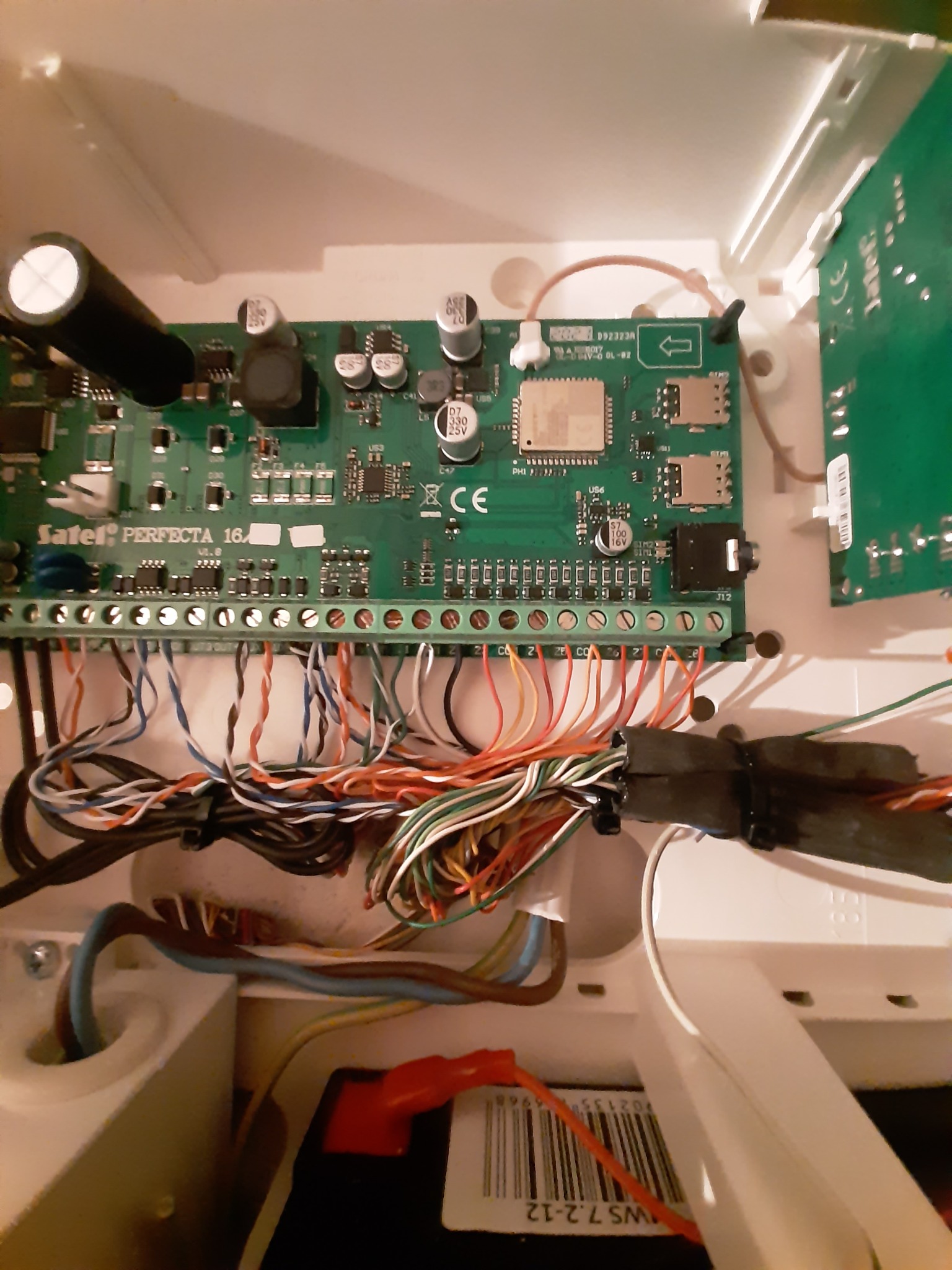 Otwarta obudowa centrali alarmowej Satel Perfecta 16A z widoczną płytą główną, licznymi przewodami podłączonymi do listwy zaciskowej i elementami elektroniki.