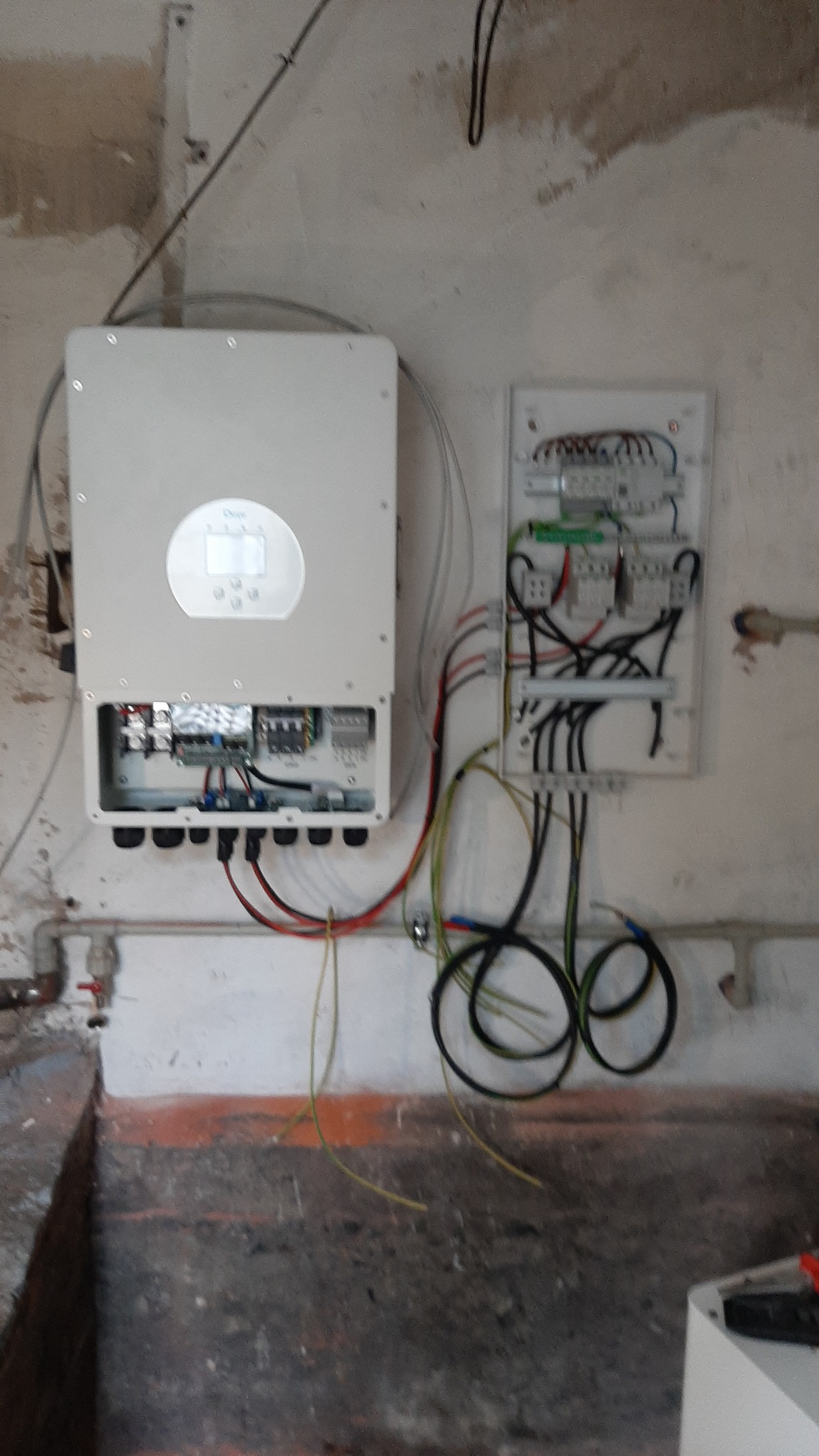 Montaż falownika i rozdzielnicy elektrycznej na surowej ścianie z widocznymi przewodami, w trakcie instalacji.