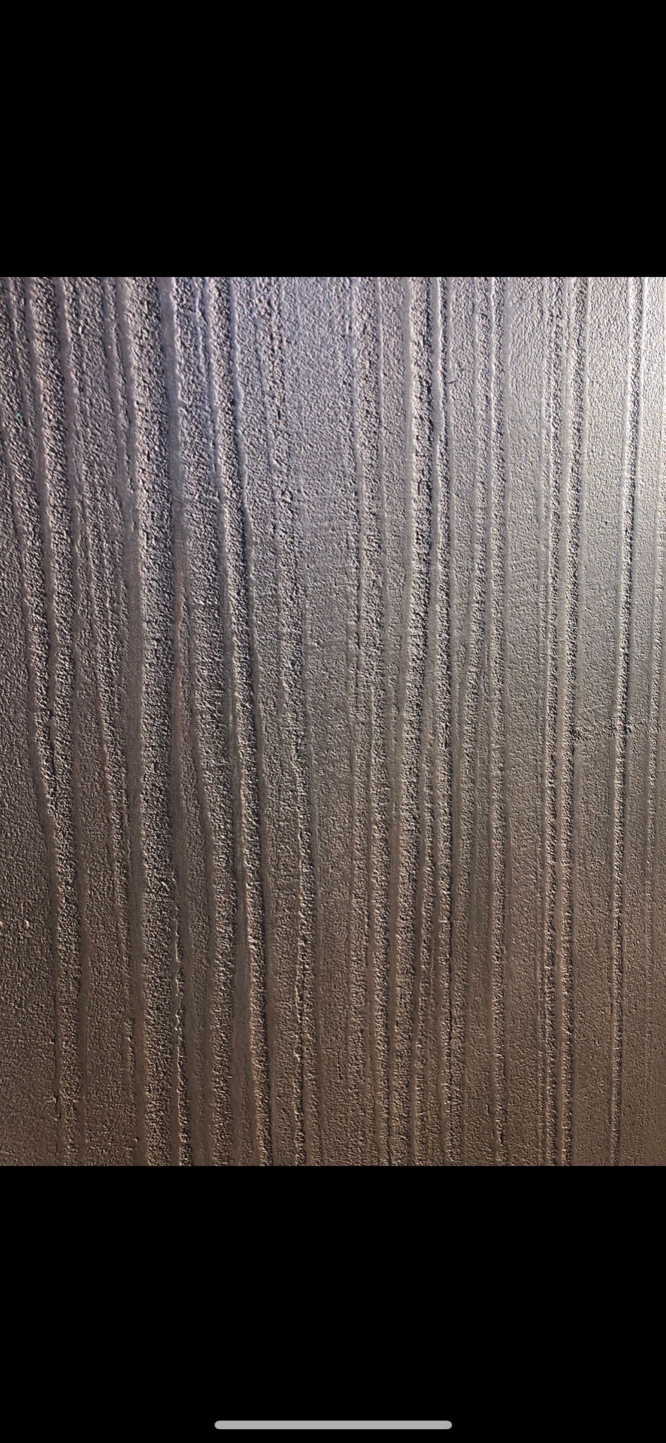 Szara ściana z pionowymi, nieregularnymi rowkami, przypominająca fakturę drewna.
