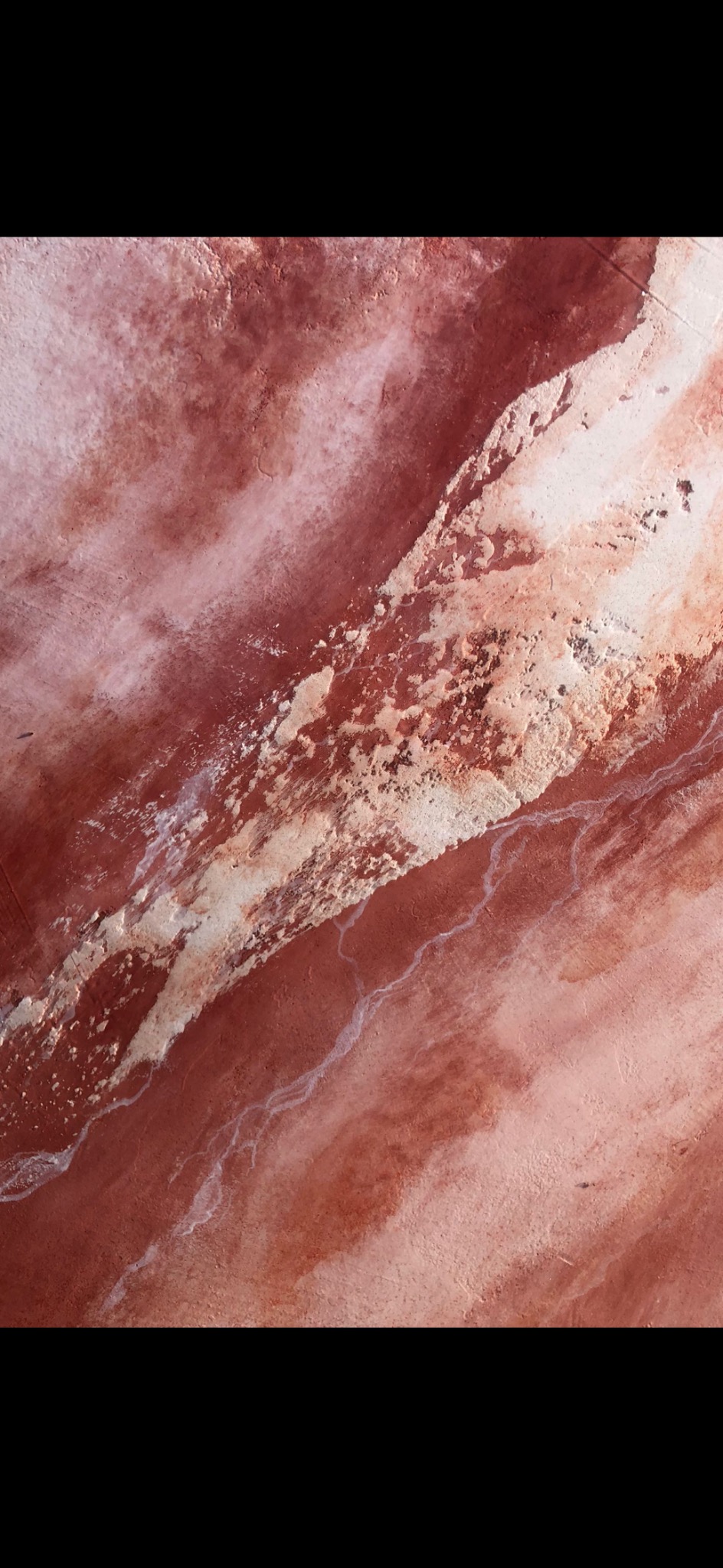 Nierówna, różowo-czerwona powierzchnia z białymi żyłkami, przypominająca surowy tynk lub grunt mineralny z widocznymi smugami i nierównościami.