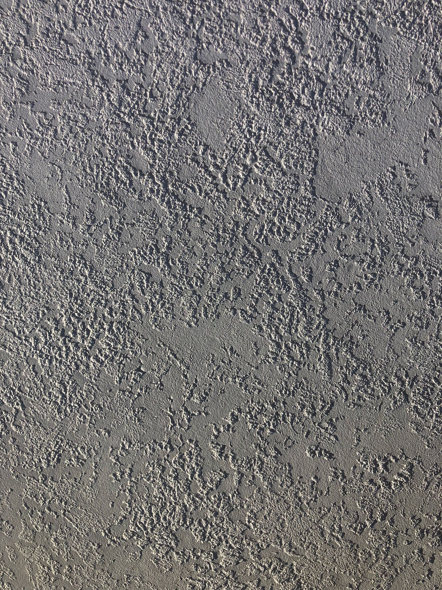 Szara, chropowata powierzchnia ściany z wyraźną fakturą, oświetlona z góry.