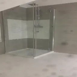 Nowoczesna kabina prysznicowa z deszczownicą, szklane drzwi, biały brodzik, płytki w odcieniach szarości z poziomymi paskami, grzejnik drabinkowy po lewej stronie.