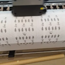 Drukarka wielkoformatowa drukuje powtarzalny wzór z logo i motywem leśnym na białym materiale.