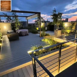 Nowoczesny taras na dachu w Warszawie oświetlony LED, z szarą nawierzchnią, metalową pergolą i roślinami ozdobnymi, sfotografowany o zmierzchu.