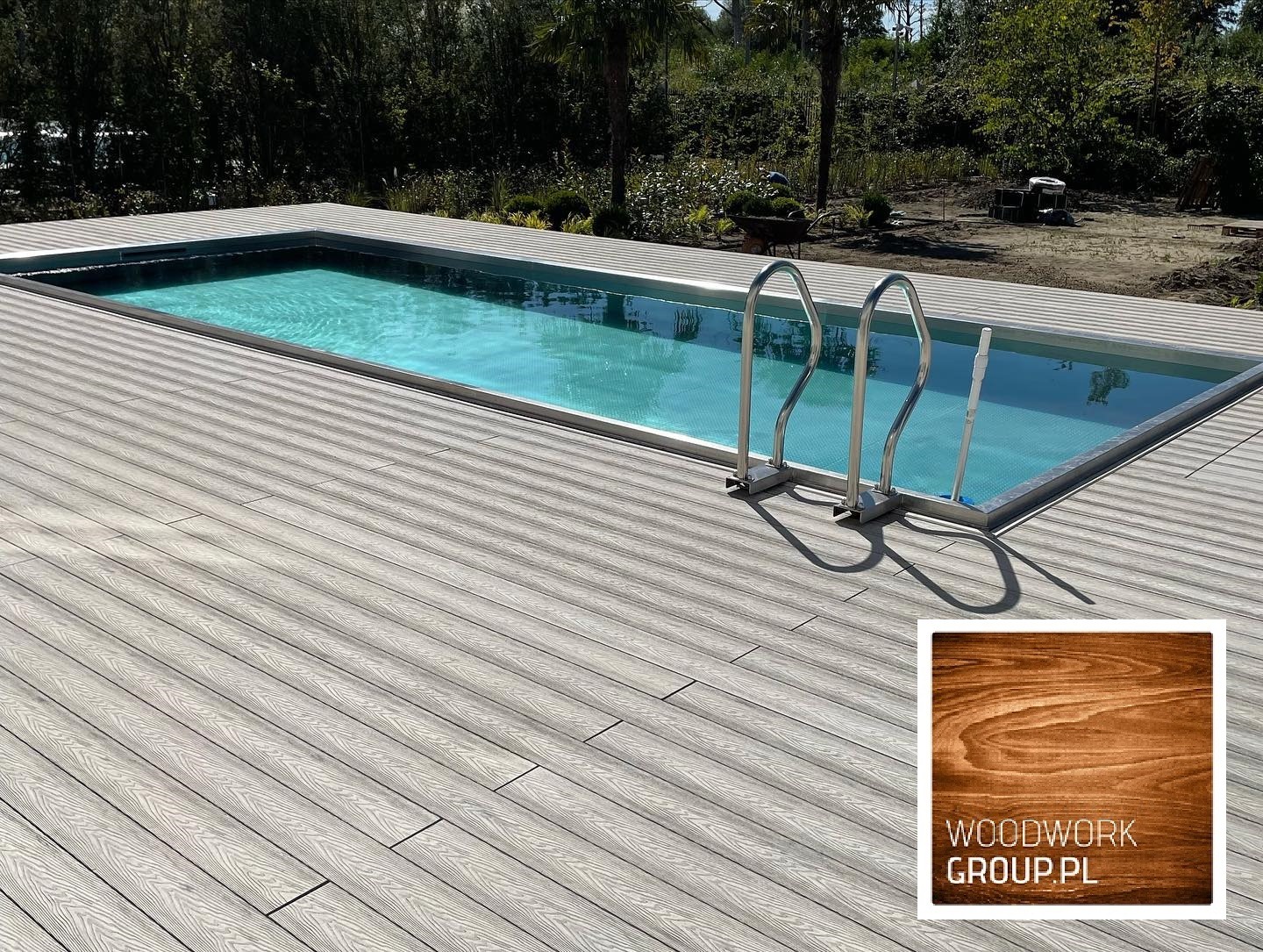 Szary taras z desek kompozytowych otaczający basen z drabinką w Warszawie, widoczny fragment logo firmy.