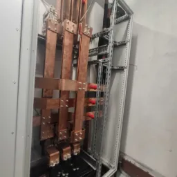 Rozdzielnica elektryczna z miedzianymi szynami i czarnymi kablami wewnątrz metalowej szafy, widok z bliska.