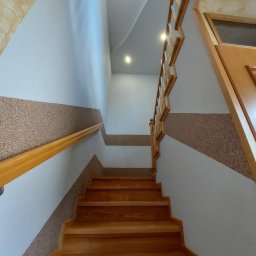 SIKOR-BUD - Klatka schodowa w domu z drewnianymi schodami, poręczą i ozdobnymi pasami na ścianach.