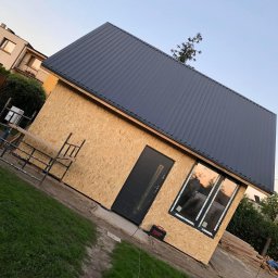 SIKOR-BUD - Niedokończony budynek gospodarczy z dachem z blachy trapezowej, ścianami z płyt OSB, wstawionymi oknami i drzwiami, widoczne rusztowanie i narzędzia.