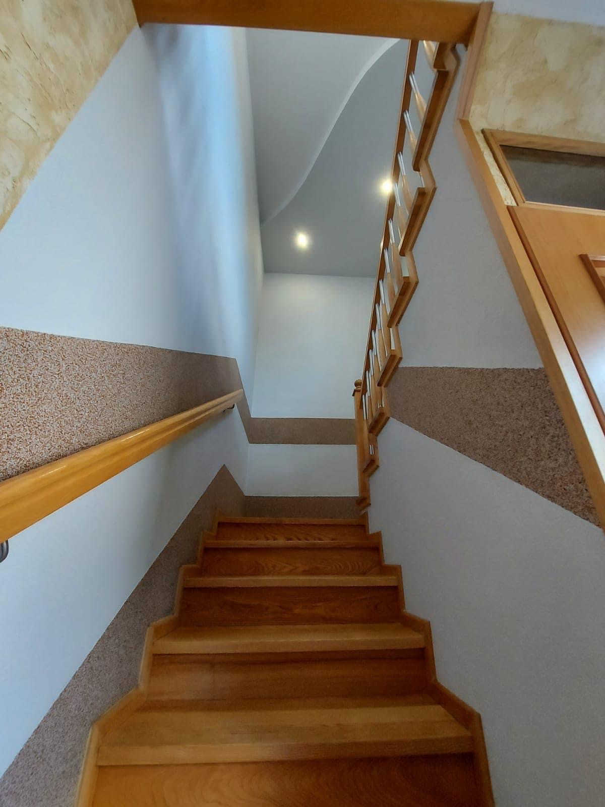 Klatka schodowa w domu z drewnianymi schodami, poręczą i ozdobnymi pasami na ścianach.