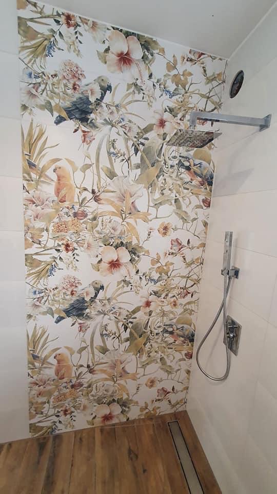 Wykończona łazienka w Oleśnicy z kabiną prysznicową typu walk-in, drewnopodobną podłogą i ścianą pokrytą tapetą w kwiaty i papugi.