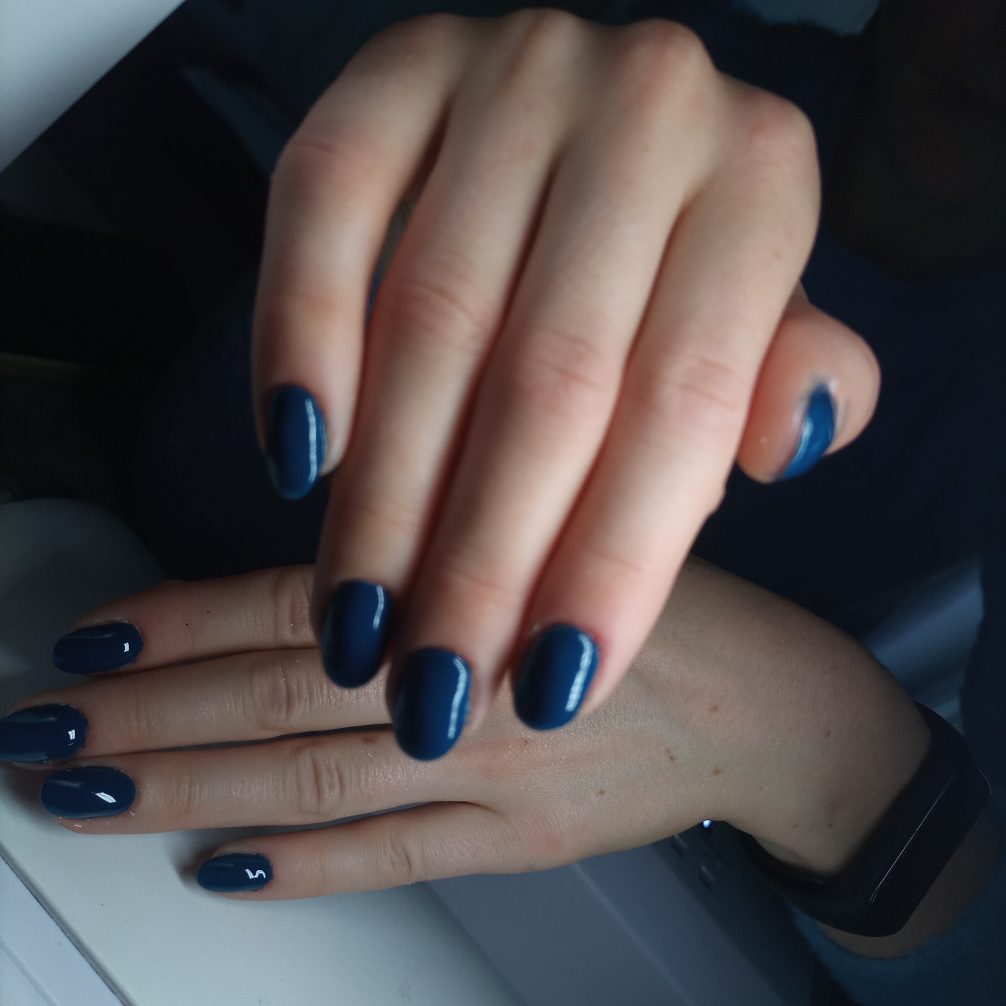 Dłonie z pomalowanymi na ciemny, granatowy kolor owalnymi paznokciami. Na jednym z paznokci widoczny biały refleks światła.