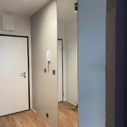 Szafa na wymiar z lustrzanymi drzwiami w przedpokoju, widoczne oświetlenie punktowe, domofon i drzwi wejściowe.