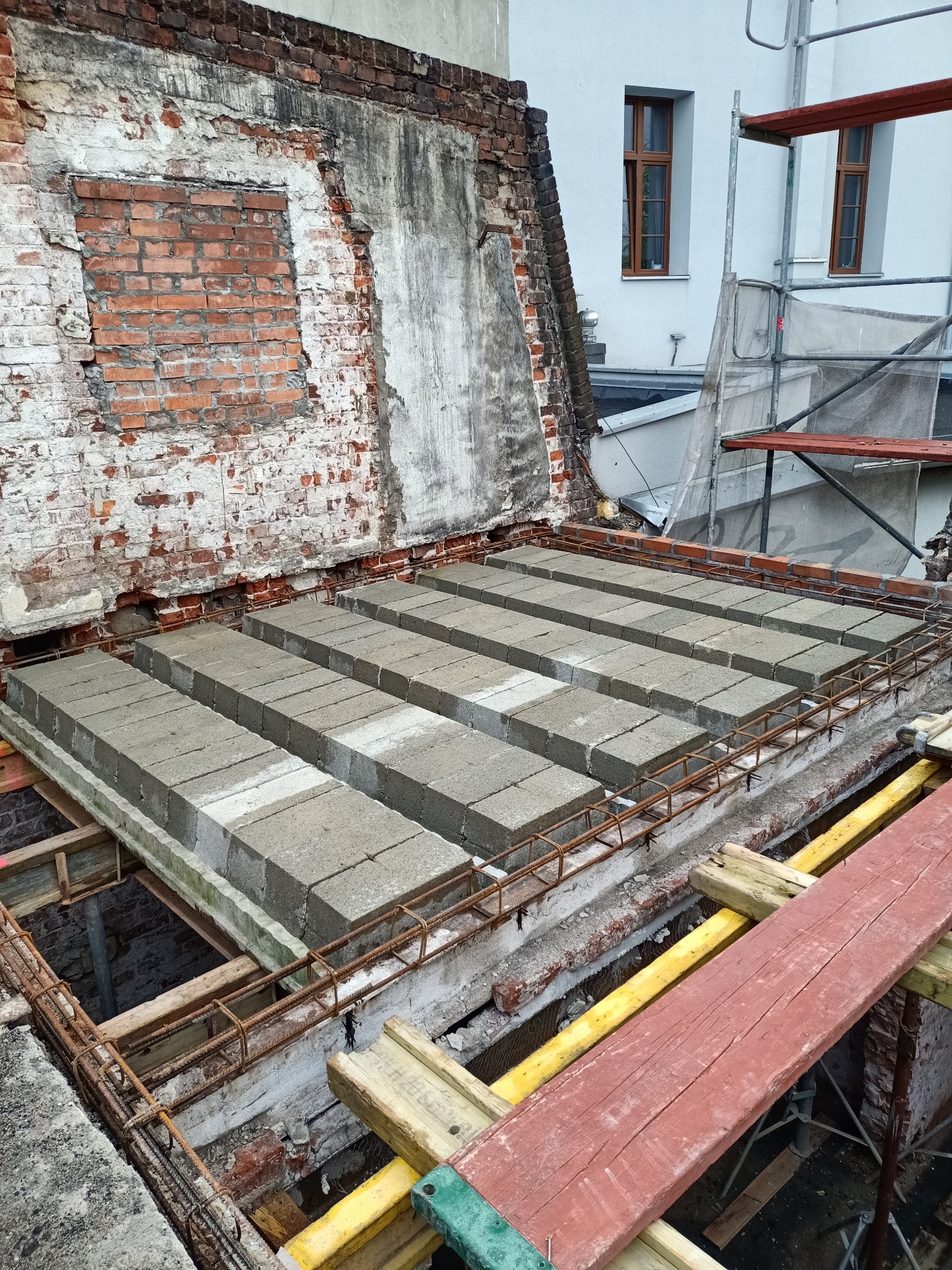 Wznoszenie stropu Teriva z pustaków betonowych na budynku z odsłoniętą cegłą i widocznym deskowaniem.