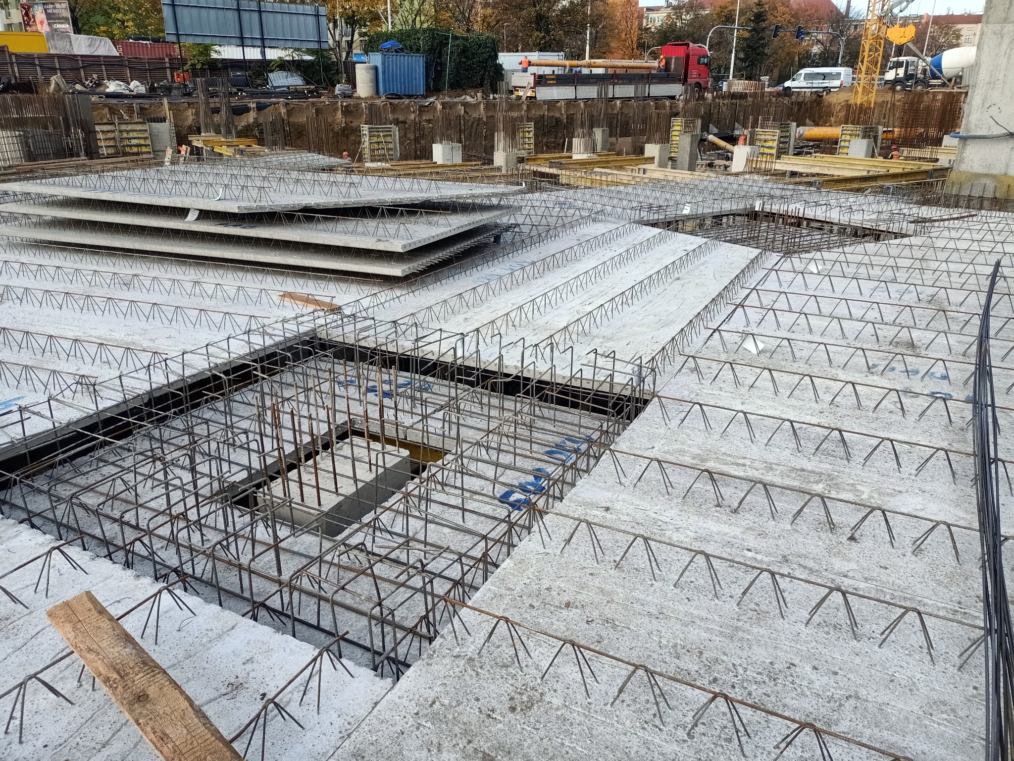 Wykonywanie płyty fundamentowej z widocznym zbrojeniem i szalunkiem, plac budowy w tle.