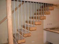 Nowoczesne schody wspornikowe z drewnianymi stopniami i metalową balustradą, zamocowane do ściany, widoczne z boku.