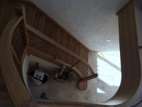 Zakrzywione, drewniane schody w trakcie montażu, widoczne elementy konstrukcyjne i narzędzia, surowe wykończenie ścian, jasne oświetlenie dzienne.