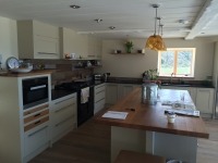 Jasna kuchnia z zabudową meblową w kształcie litery U, z drewnianym blatem na wyspie kuchennej i czarnym sprzętem AGD, widok z perspektywy podłogi.