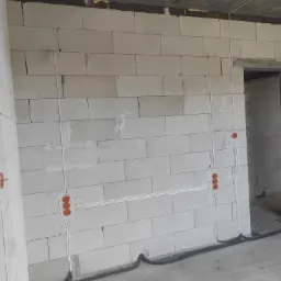 Surowa ściana z betonu komórkowego z widocznymi przewodami elektrycznymi i puszkami instalacyjnymi w trakcie montażu instalacji elektrycznej w Siedlcach.
