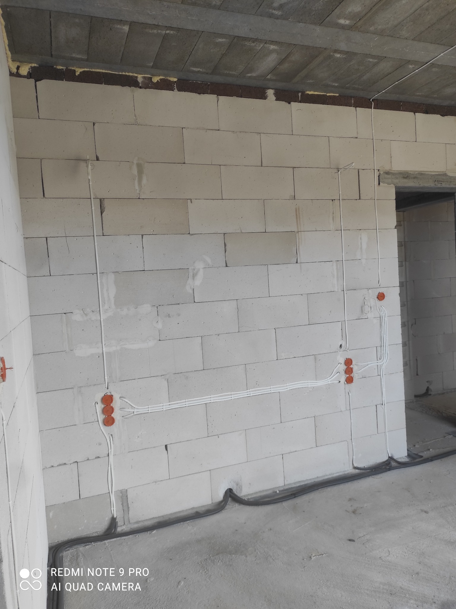 Surowa ściana z betonu komórkowego z widocznymi przewodami elektrycznymi i puszkami instalacyjnymi w trakcie montażu instalacji elektrycznej w Siedlcach.
