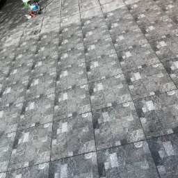 Ułożona nawierzchnia z szarych, kwadratowych płytek imitujących kamień, widoczne wiaderka z zaprawą i narzędzia do fugowania na krawędzi.