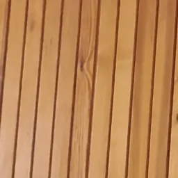 Bliski kadr na drewnianą boazerię w ciepłym, miodowym odcieniu, z widocznymi naturalnymi słojami i sękami, tworzącymi pionowe linie.