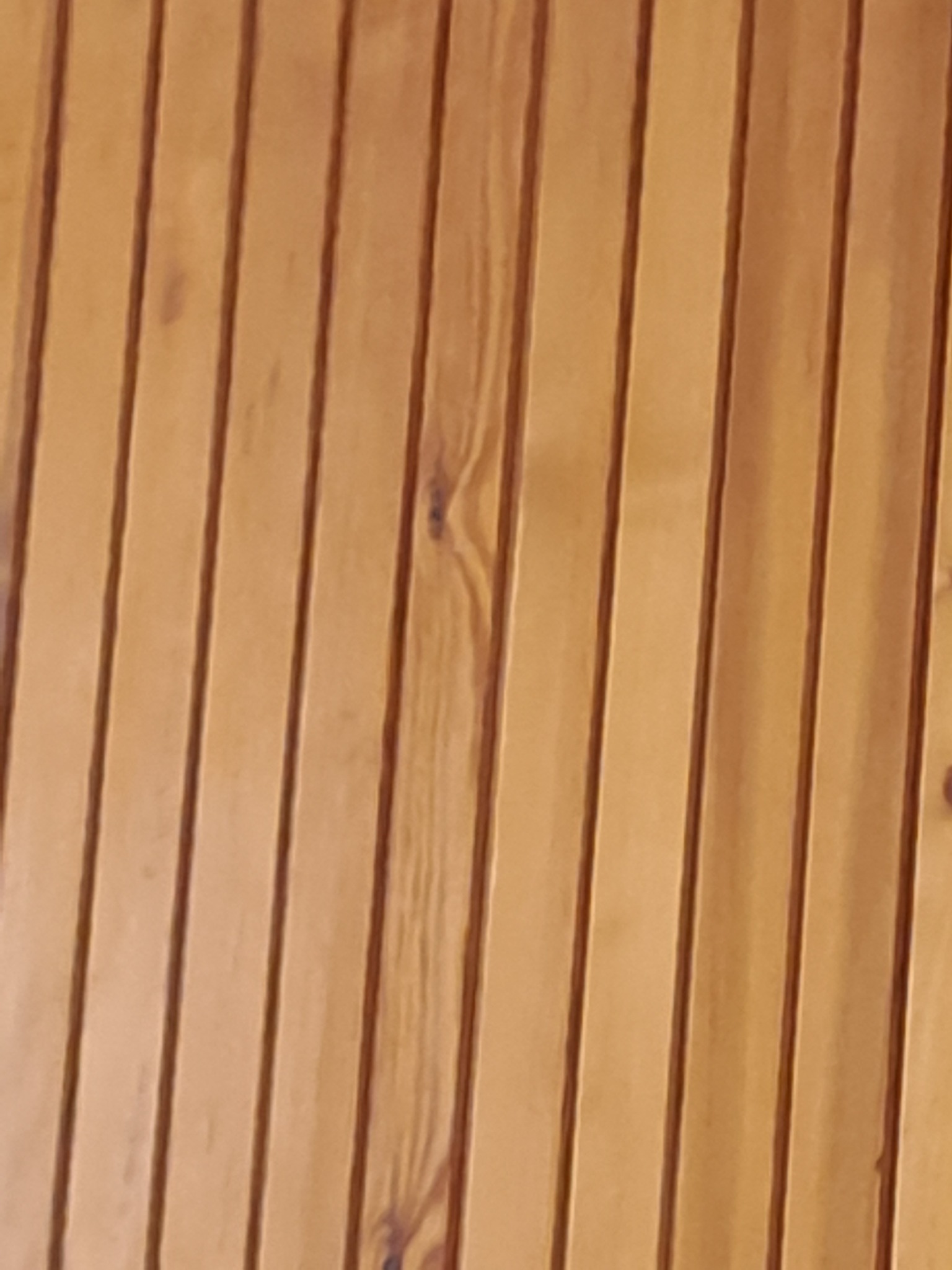 Bliski kadr na drewnianą boazerię w ciepłym, miodowym odcieniu, z widocznymi naturalnymi słojami i sękami, tworzącymi pionowe linie.