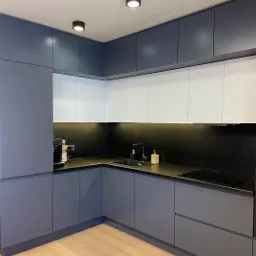 Nowoczesna kuchnia na wymiar w odcieniach szarości i bieli, z minimalistycznym czarnym blatem i drewnianą podłogą, oświetlona punktowymi lampami sufitowymi.