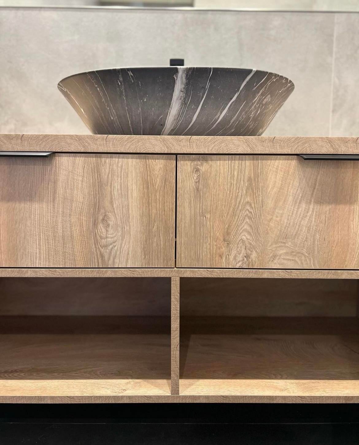 Łazienkowa szafka z drewnopodobnym fornirem i umywalką w kształcie misy z szaro-białego marmuru.