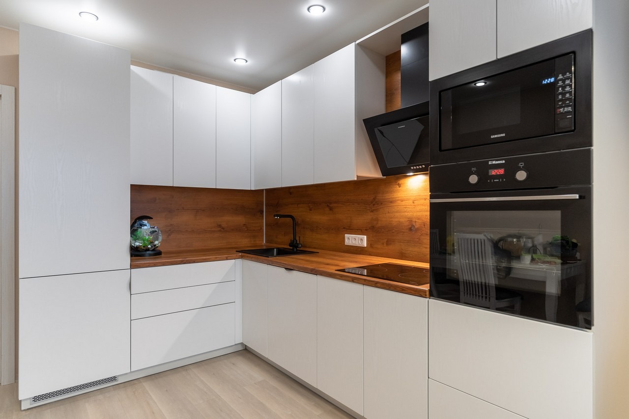 Nowoczesna kuchnia z białymi szafkami, drewnianym blatem i panelem ściennym, czarną armaturą i akwarium na blacie.