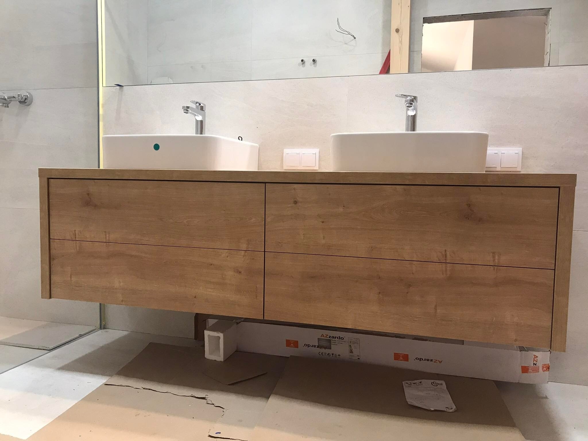 Wisząca szafka łazienkowa z dwiema umywalkami nablatowymi i drewnianymi frontami szuflad w trakcie montażu, widoczne kartony producenta Azzardo pod szafką.