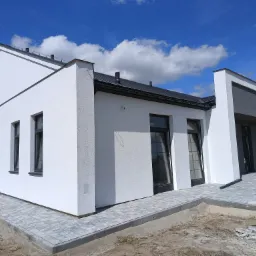 Nowoczesny, biały dom z szarą kostką brukową na podjeździe, widok z niskiej perspektywy, błękitne niebo z chmurami w tle.