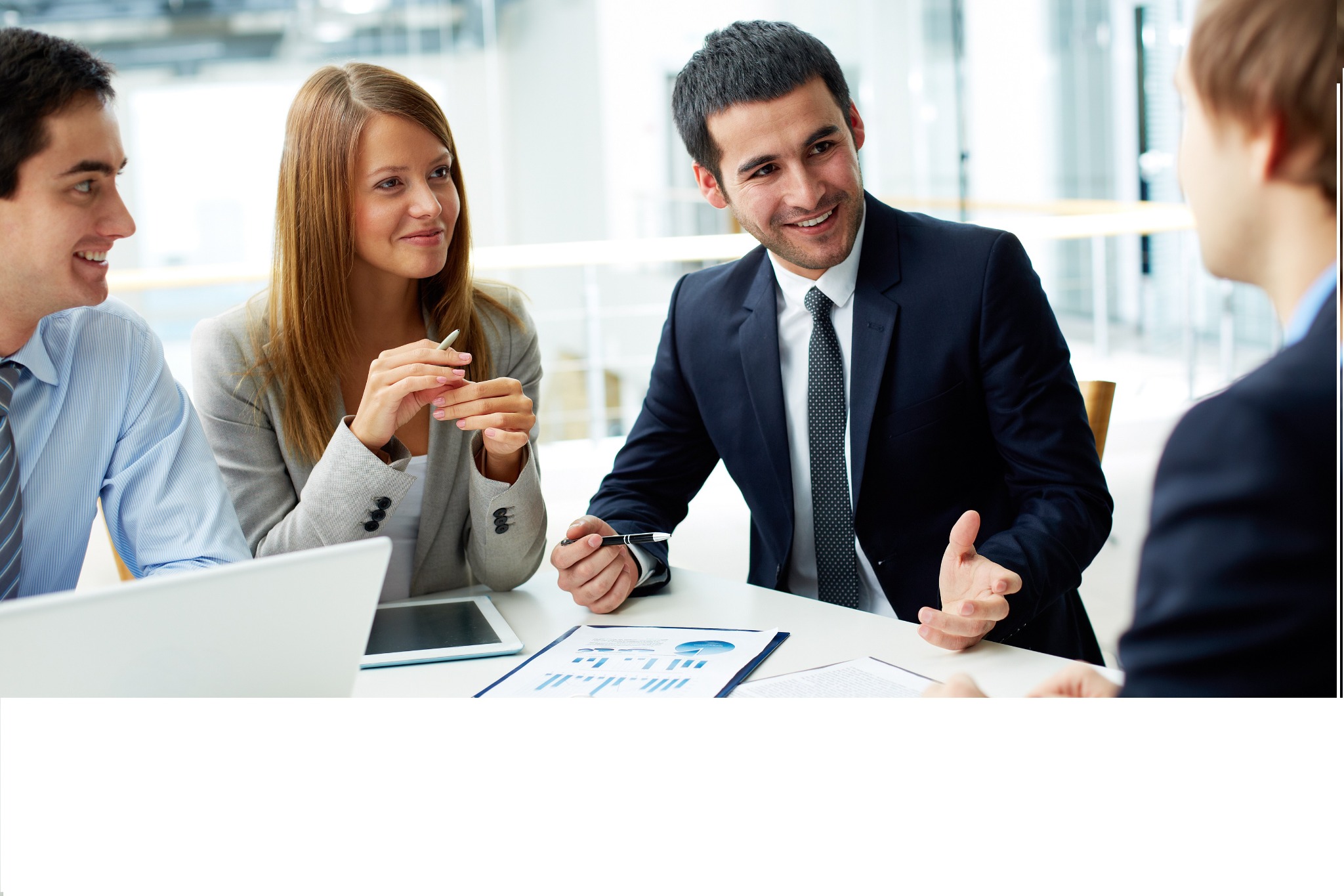 Czterech profesjonalistów w strojach biznesowych omawia wykresy na dokumencie, z laptopem i tabletem na stole podczas spotkania w jasnym biurze.