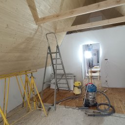 BUDROB - Poddasze w trakcie prac wykończeniowych: drewniana boazeria na suficie, drabina, odkurzacze, widoczny etap prac remontowych. Surowy stan podłogi, instalacja elektryczna.