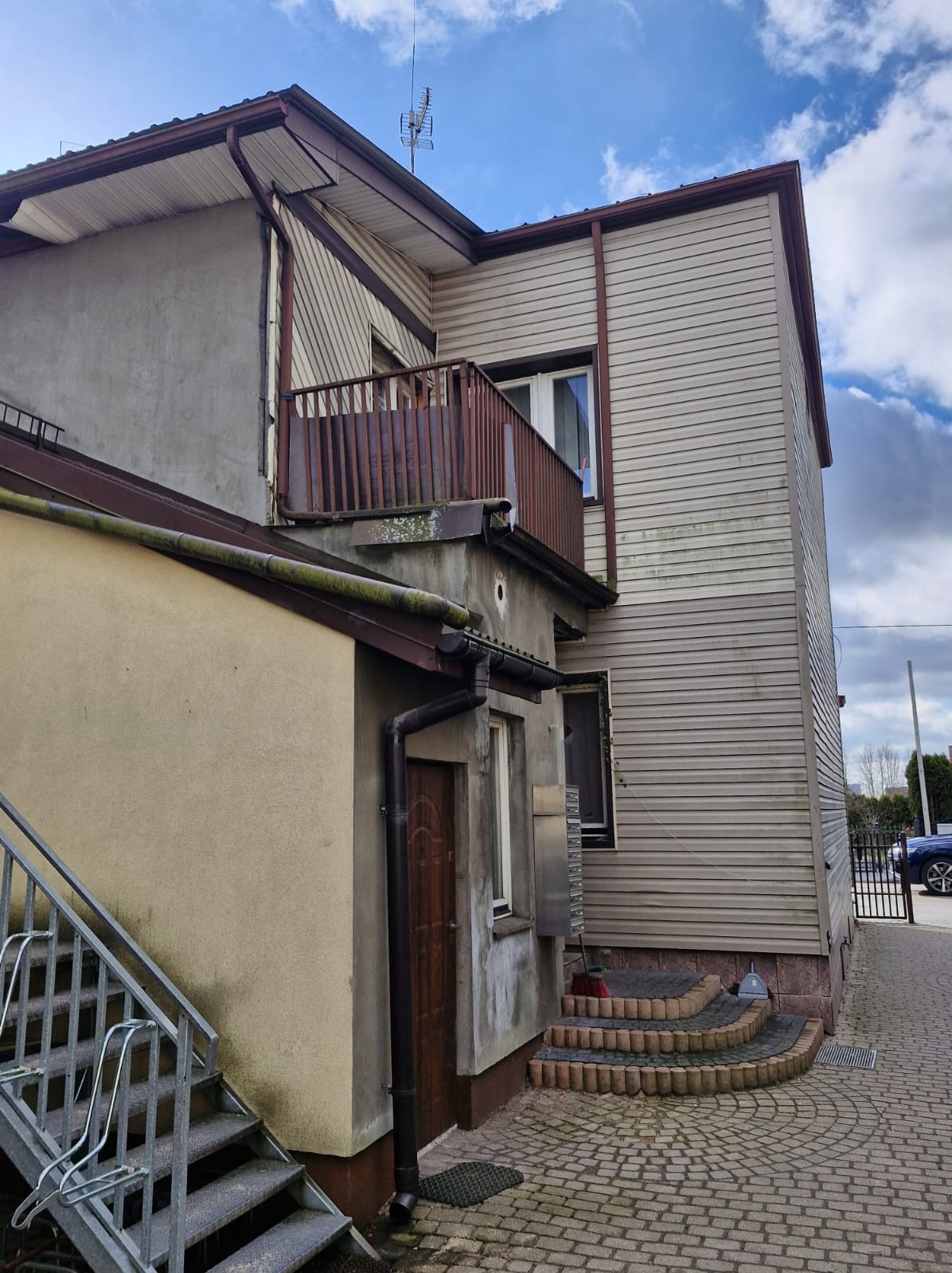 Elewacja dwupiętrowego budynku z balkonem w Augustowie. Widoczna drewniana boazeria, okna i schody wejściowe. Ujęcie z dołu podkreśla bryłę budynku.