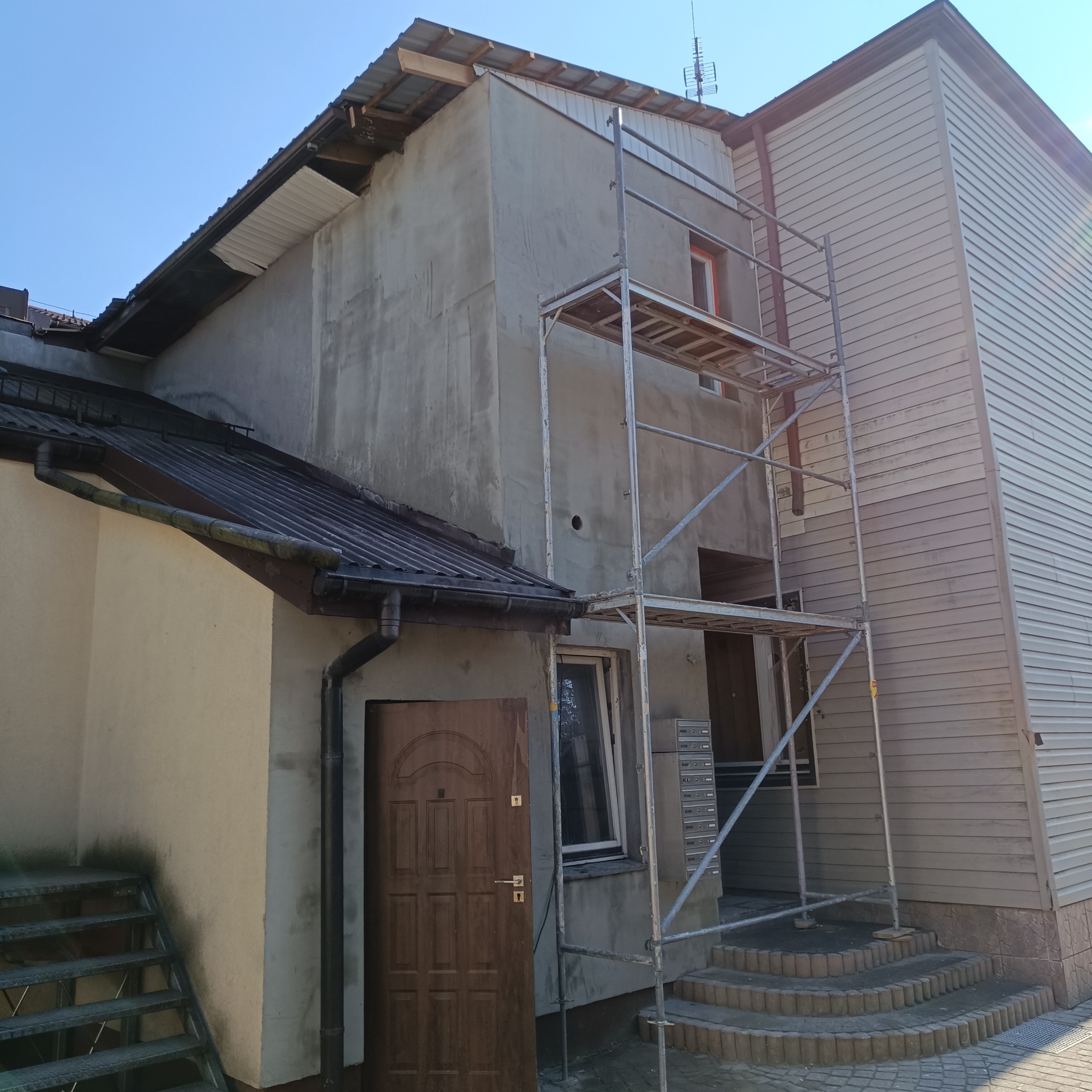 Elewacja budynku w trakcie prac remontowych. Widoczne szpachlowanie, rusztowanie i fragment sidingu. Ujęcie z dołu, w dziennym świetle.