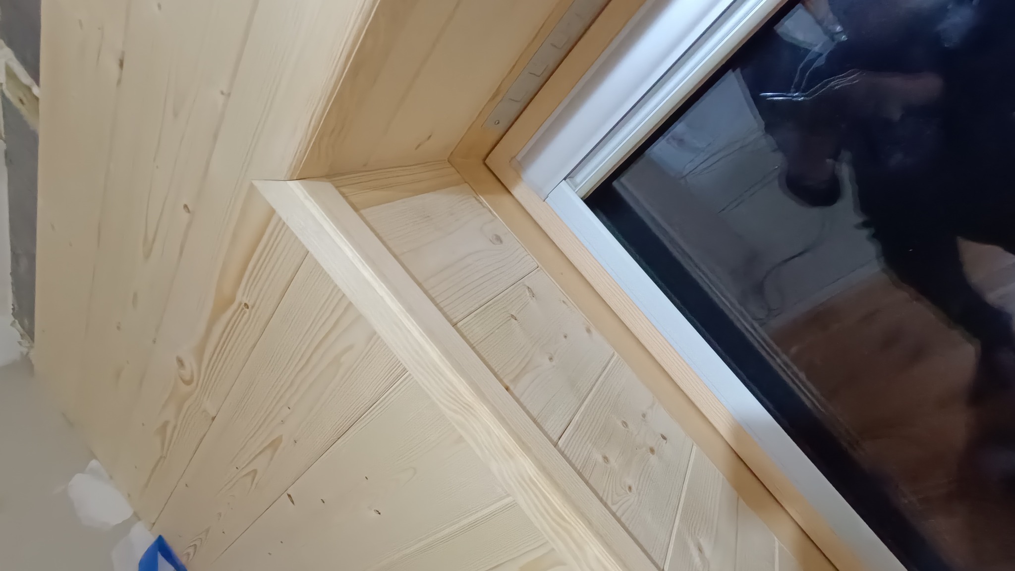 Wykończenie drewnianej boazerii wokół okna dachowego, widoczne detale połączeń i struktura drewna, surowe wykończenie, etap prac wykończeniowych.