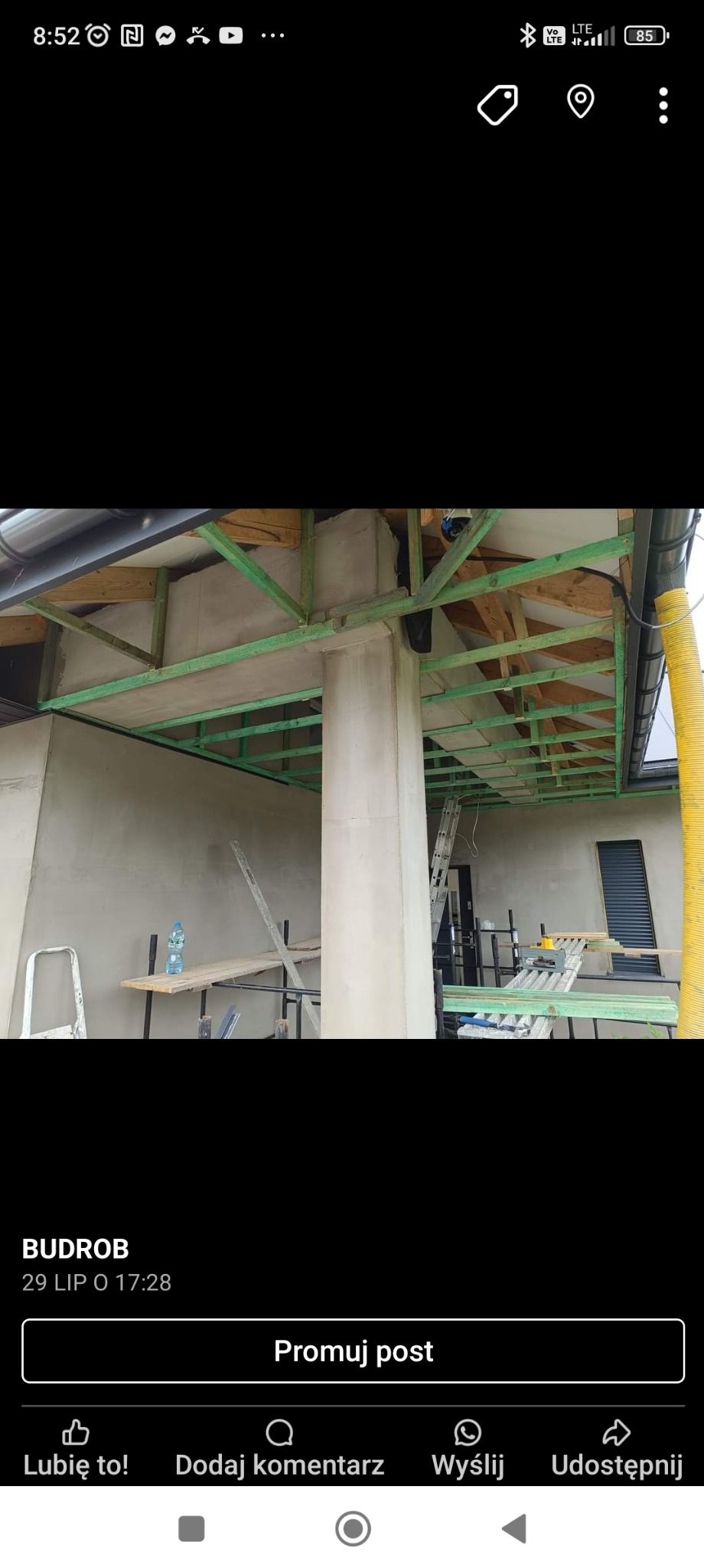 Wnętrze w trakcie prac wykończeniowych: surowa ściana, drewniana konstrukcja pod sufitem pomalowana na zielono, kolumna. Widoczne rusztowania i narzędzia.