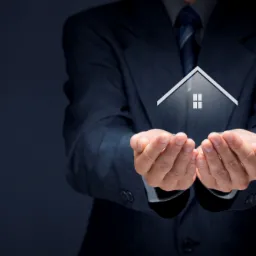 Mężczyzna w garniturze trzyma w dłoniach symbol domu z dwoma oknami, prezentacja oferty.