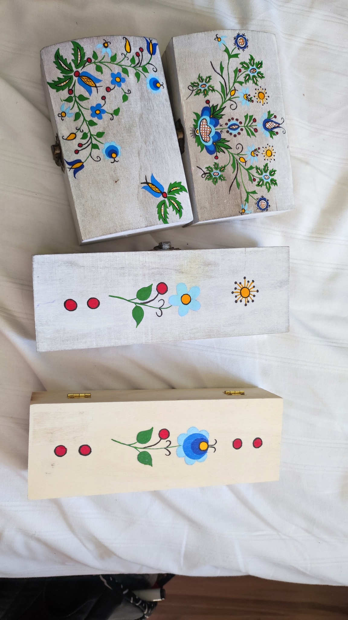 Ręcznie malowane, drewniane szkatułki z motywami kwiatowymi w stylu ludowym, leżące na białym materiale.