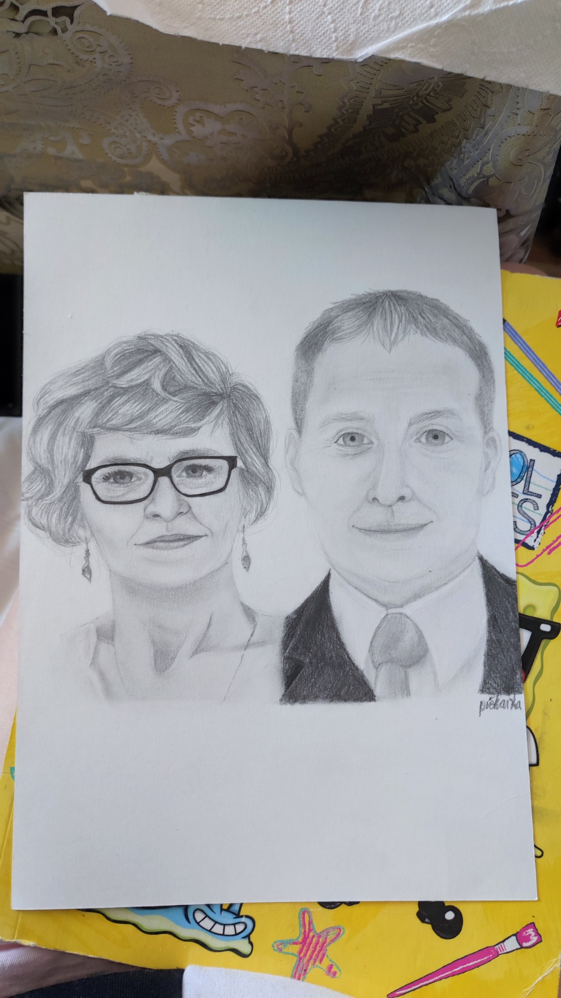 Ręcznie rysowany ołówkiem portret kobiety w okularach i mężczyzny w garniturze, z sygnaturą artysty w prawym dolnym rogu.